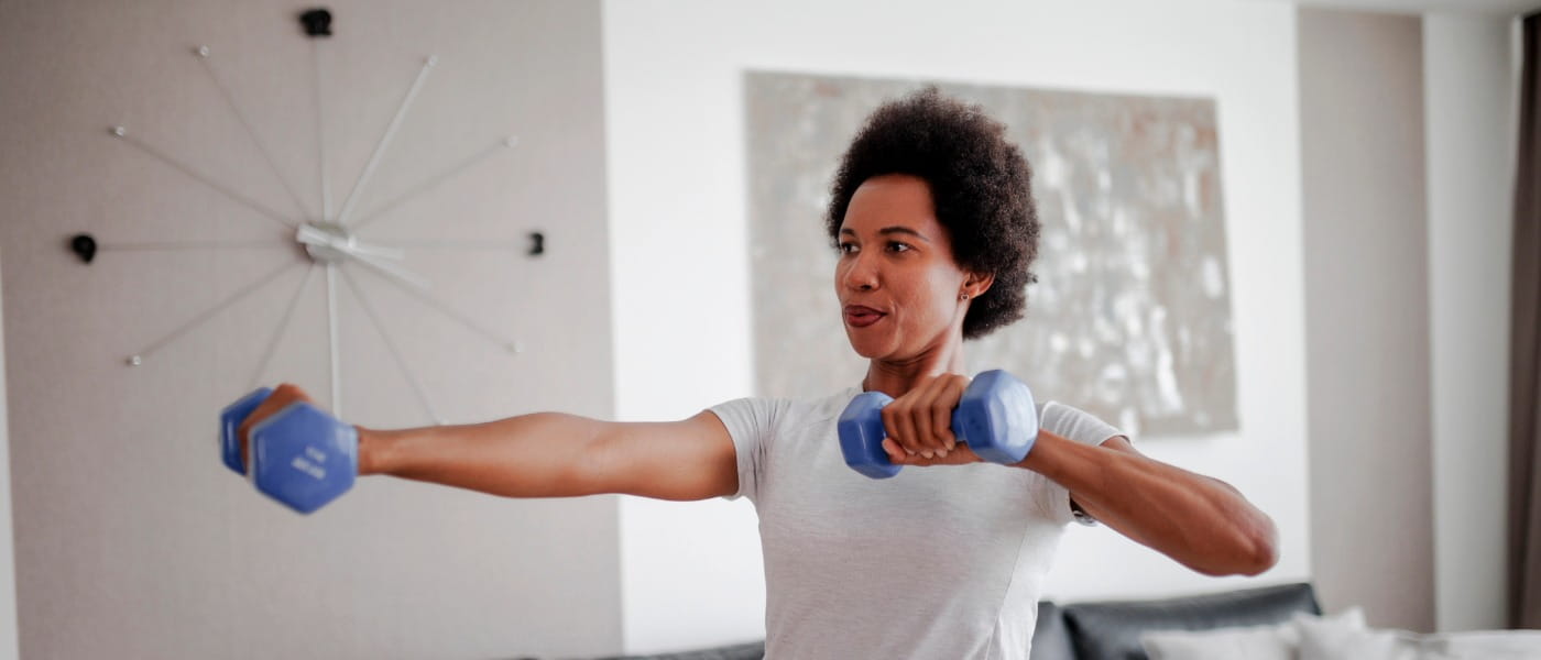 middle aged woman of color doing punches using dumbbells in her living room