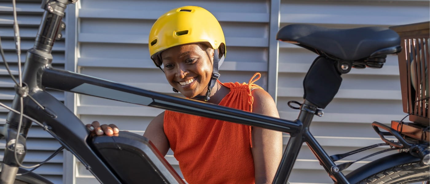 older teenage girl wearing a helmet adjusting the battery on her e-bike