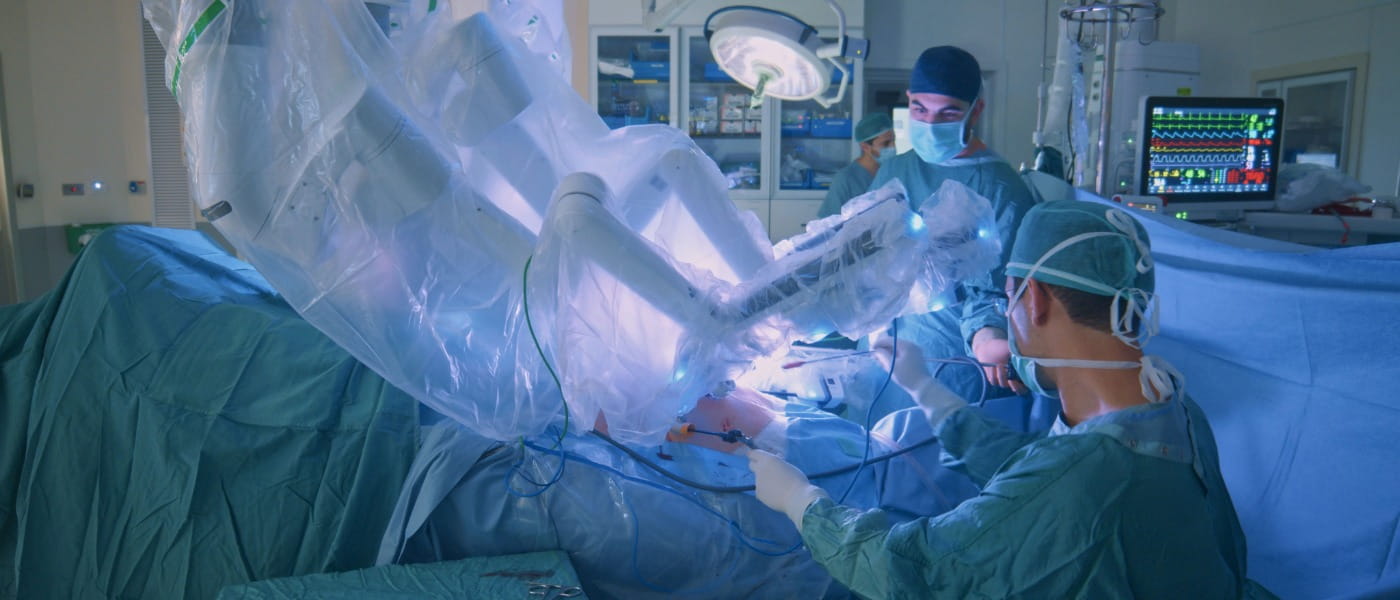 Three male surgeons preparing to treat an adult's torso in a hospital operating room.