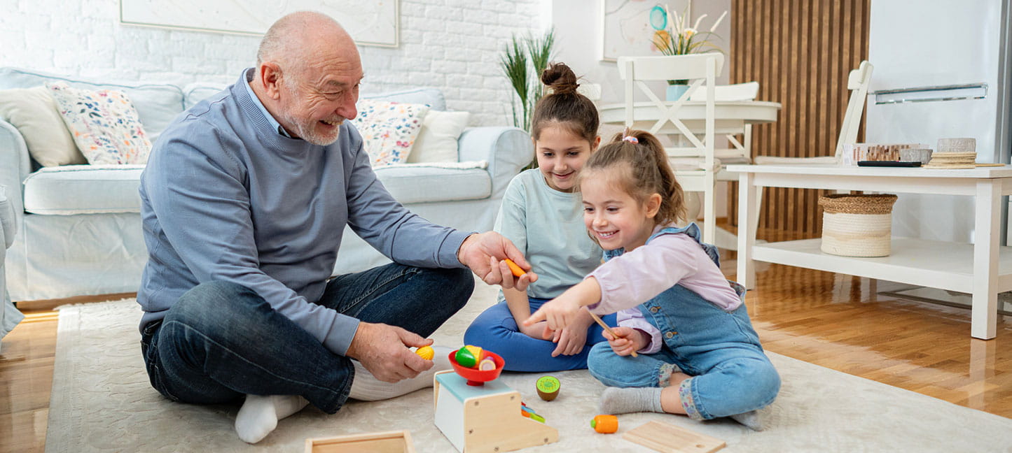 Caucasian grandfather enjoying playtime with his two young granddaughters on the living room floor.