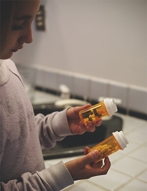 adolescent girl with access to prescription medicines holding two pill bottles