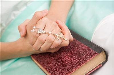 Hands folded over a bible holding a rosary