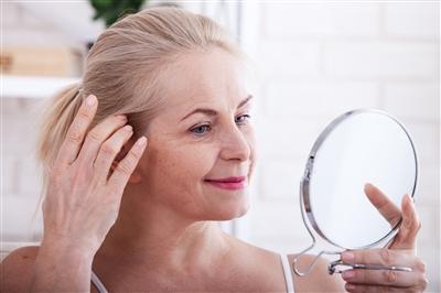 Woman looking at her face in a hand mirror