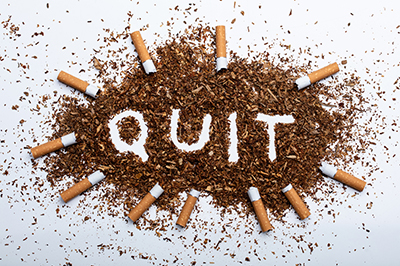Cigarette butts and pile of tobacco with the word quit written in the pile
