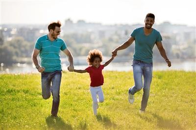 Two fathers and daughter running outside