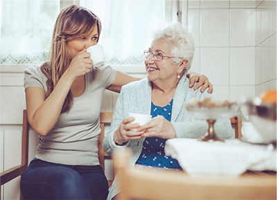 An older and middle aged woman sitting together enjoying a cup of coffee
