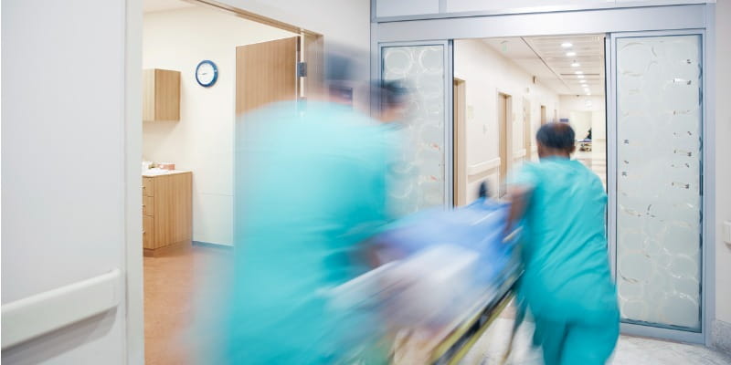 Hospital clinicians wheeling bed through hallway