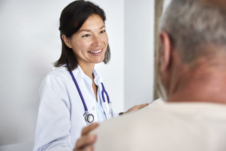 Over the shoulder view of smiling female medical professional. Doctor is consoling patient. She is wearing lab coat.