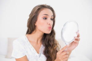 woman performing facial yoga while looking in a hand mirror