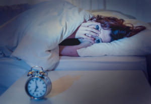 woman lying in bed awake looking at clock through her hand on her face