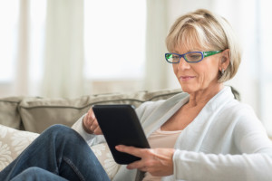 older woman using a tablet while lounging on couch
