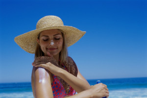 woman on a beach in a sunhat applying sunscreen to her arm